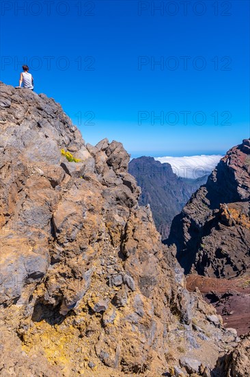 A young woman sits resting and looking at the views of the Roque de los Muchachos national park on top of the Caldera de Taburiente