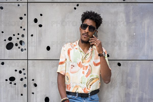 Cool african american young man talking to the mobile leaning on an urban wall