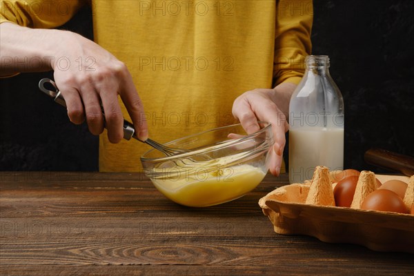 Unrecognizable man whisking eggs with milk for omelette