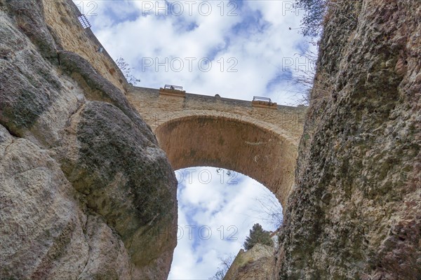 View from below a stone bridge over a cliff in the background a blue sky with clouds in ronda