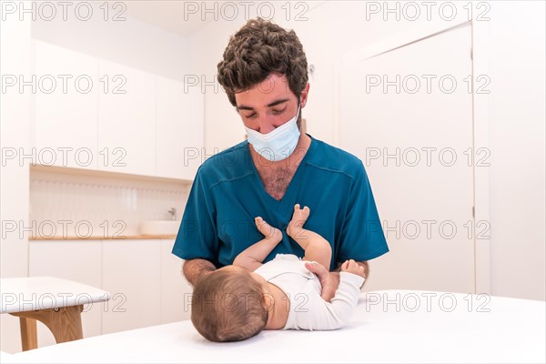 Portrait of a young doctor checking up a baby lying down on stretcher in a clinic