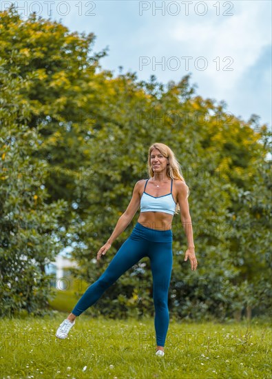 Fitness session with a young blonde Caucasian woman exercising on the street with a blue maya on her feet and a white short shirt. Performing side jumps