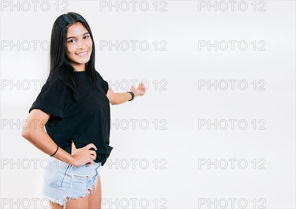 Happy young girl welcoming you isolated. Smiling latin girl pointing back presenting a product. Latin girl pointing a promotion with her palm