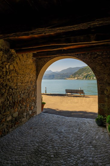 Old Beautiful Street Tunnel with Arch and a Bench from Brusino Arsizio on the Waterfront in a Sunny Summer Day and with Lake Lugano and Mountain View over Morcote
