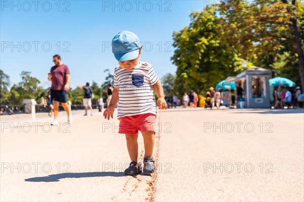 Portrait of a one year old Caucasian boy looking at the camera walking in a park with a cap