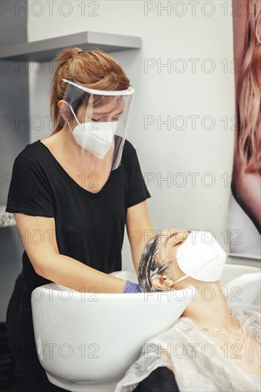 Hairdresser with mask and gloves washing the client's hair with soap. Reopening with security measures of Hairdressers in the Covid-19 pandemic