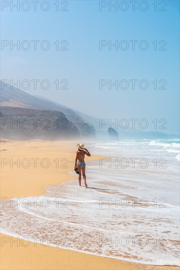 A young tourist with a hat walking alone on the Cofete beach of the Jandia natural park