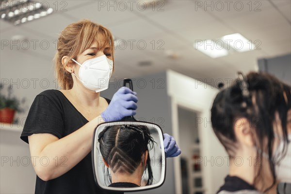 Hairdresser with mask showing the result of the cut in a mirror. Reopening with security measures of Hairdressers in the Covid-19 pandemic