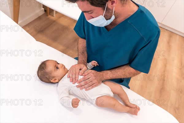 High angle view of a Doctor with facial mask examining a baby in a clinic