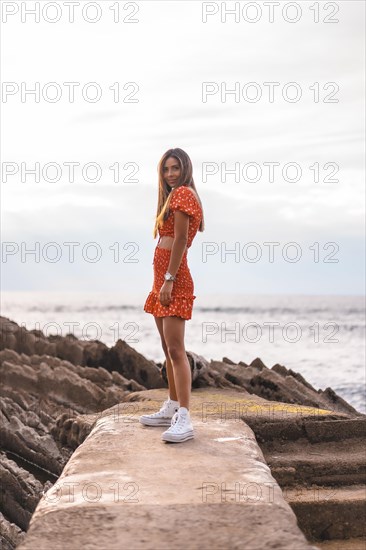 A young brunette Caucasian woman in a red dress on the beach of Itzurrun in the town of Zumaia