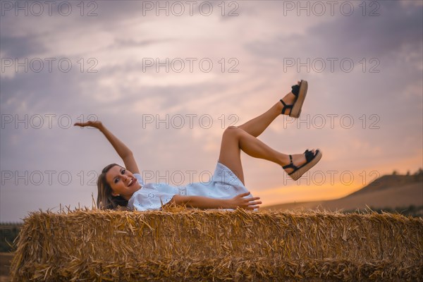 A young blonde Caucasian woman in a white dress in a field of dry straw atop a haystack. In a dry cultivated field in Navarra