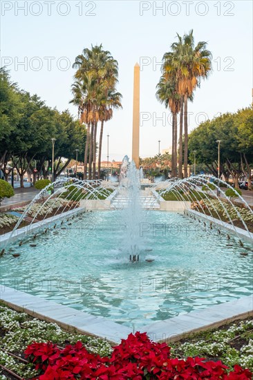 Water fountain and flowers next to palm trees on Las Belen street of Rambla de Almeria at sunset