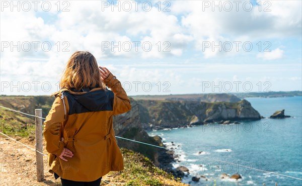 A young woman looking out to sea on the shoreline next to the Fort des Capucins a rocky