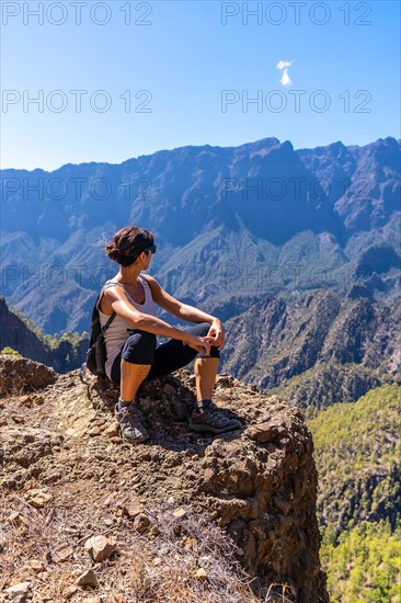 A young woman resting after trekking on top of La Cumbrecita sitting in the natural viewpoint looking at the mountains of the Caldera de Taburiente