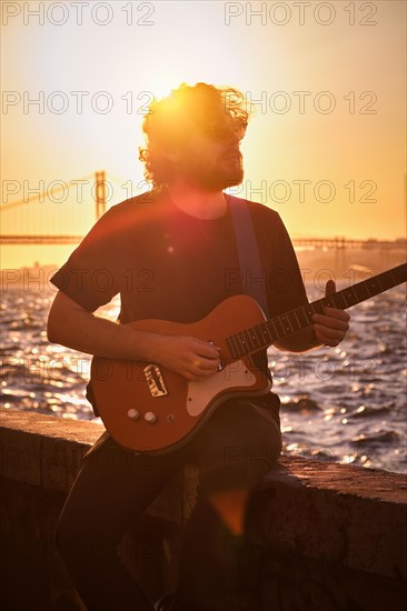 Hipster street musician in black playing electric guitar in the street on sunset