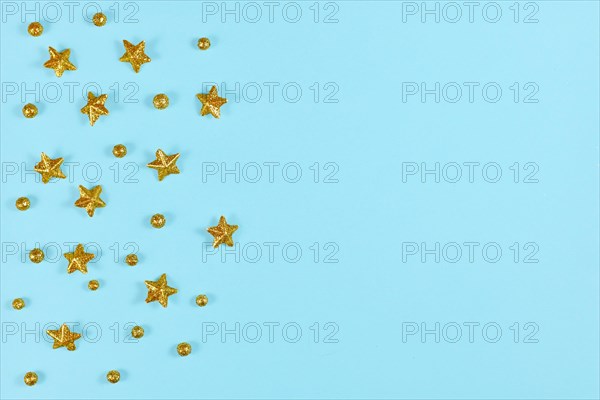 Christmas flat lay with golden stars and ball ornaments on side of light blue background with empty copy space