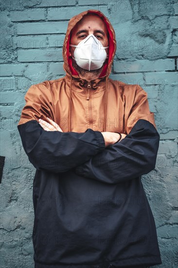 A young man in mask and hood leaning against a wall staring intently. First walks of the uncontrolled Covid-19 pandemic