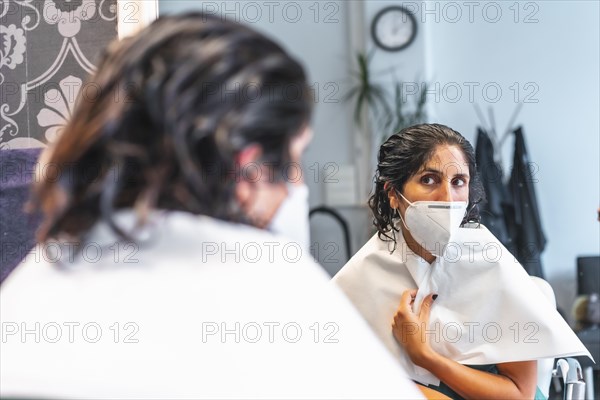 Client with face mask looking in the mirror. Safety measures for hairdressers in the Covid-19 pandemic. New normal