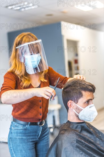 Hairdressers after the Coronavirus pandemic. Hairdresser with face mask and protective screen