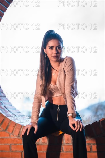 Portrait of a Caucasian brunette model sitting in the city with a beautiful ponytail and a pink sweater. Street style fashion