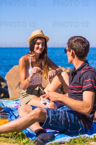 A young Caucasian couple eating some ham at the picnic in the mountains by the sea enjoying the heat