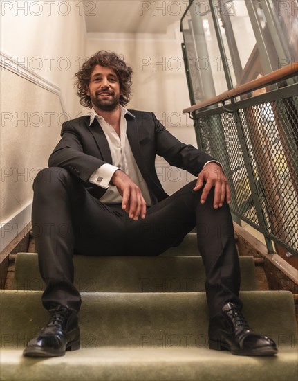 Street style with a young dark-haired caucasian man in a black suit and a white shirt in a luxurious hotel