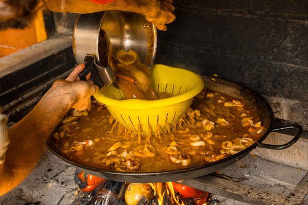 Adding fish broth to the Valencian paella with embers and vegetables. Traditional Spanish food