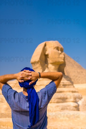 A young tourist enjoying and admiring the Great Sphinx of Giza dressed in blue and a blue turban. Cairo