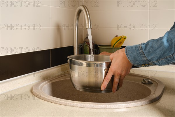 Unrecognizable woman draws water from the tap into a casserole