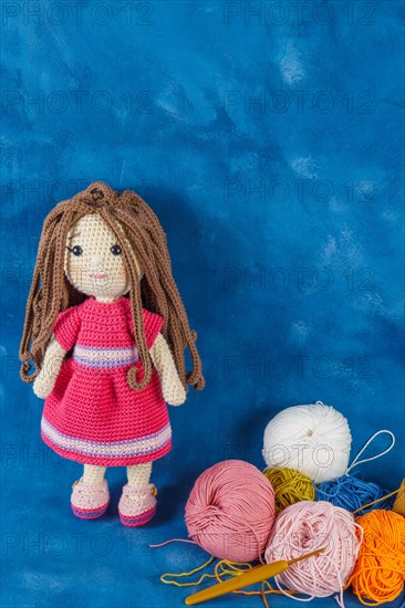 Amigurumi doll handmade on a blue background with the yarns used for its elaboration