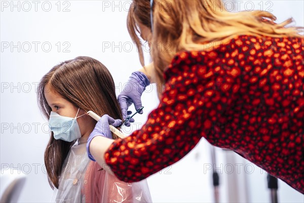 Hairdresser with mask and gloves combing the straight hair of a blonde girl