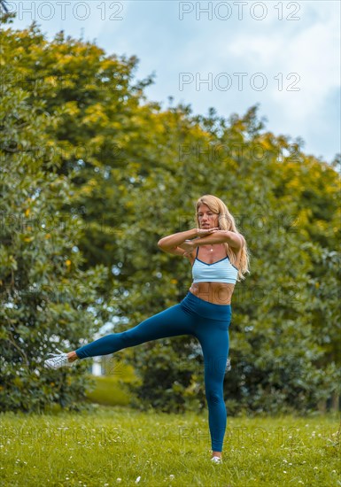 Fitness session with a young blonde Caucasian woman exercising on the street with a blue maya on her feet and a white short shirt