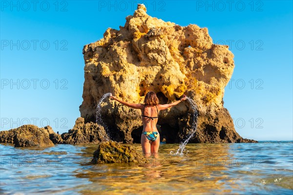 A woman on vacation throwing water at Praia dos Arrifes