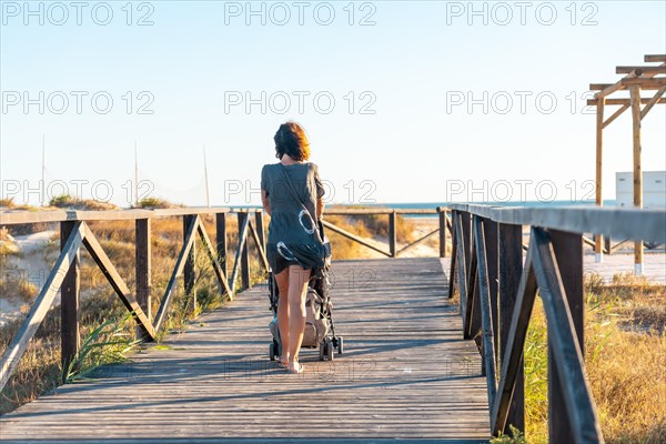 A young mother walking on the walkway of the Bateles beach in Conil de la Frontera