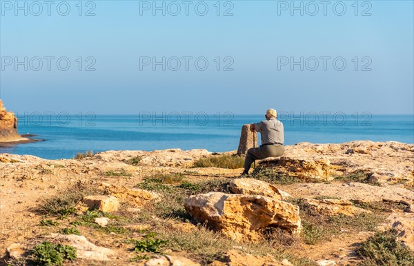 Beautiful place where is a pensive old man with a beret sitting and with a cane on the coast looking at the sea. Traditional lord of Spanish culture