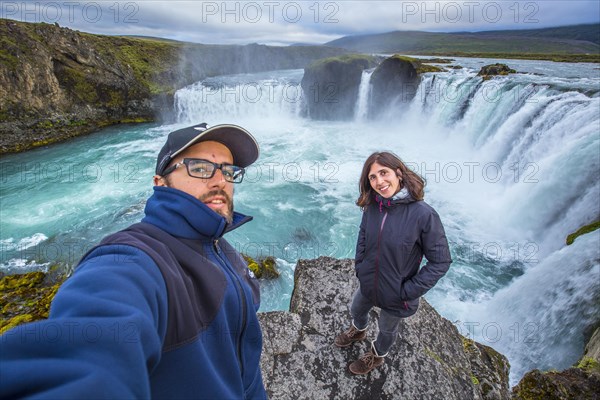 A young couple tourist looking at the Godafoss waterfall from above. Iceland