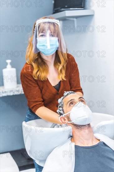 Hairdressers after the Coronavirus pandemic. Caucasian hairdresser with face mask and protective screen