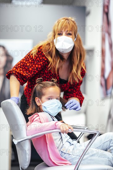 Hairdresser with mask and gloves finished the pigtails to a girl. Reopening with security measures for hairdressers in the Covid-19 pandemic