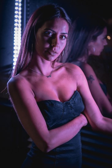A young brunette Caucasian woman in a black dress illuminated by purple LED lights