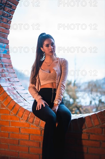 Caucasian brunette model sitting with a beautiful ponytail and a pink sweater. Street style fashion