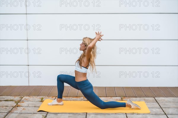 Yoga with blonde caucasian girl exercising on a yellow mat with a white wall in the background