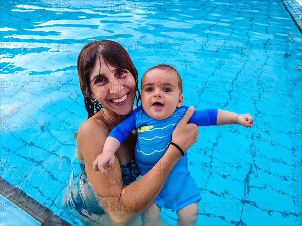 A young Caucasian mother with her baby enjoying the summer bathing for the first time in a pool
