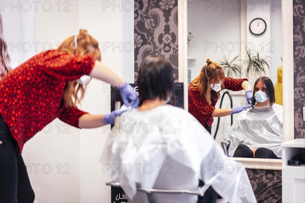 Hairdresser with mask and gloves cutting the ends to the client