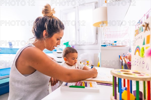 Young Caucasian mother playing with her in the room with toys. Baby less than a year learning the first lessons of her mother. Painting with color paints