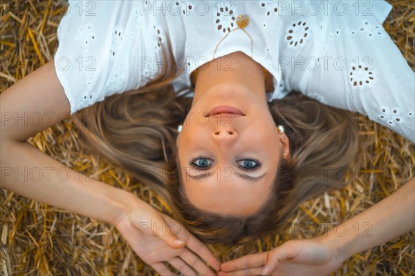 A young blonde Caucasian woman in a white dress in a field of dry straw atop a haystack. In a dry cultivated field in Navarra