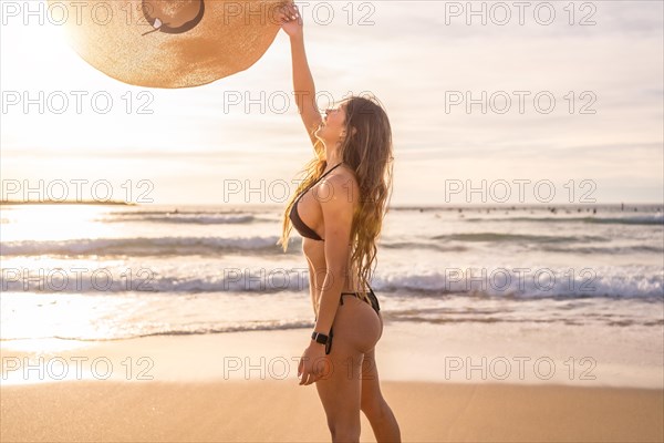 Beauty slim woman in bikini playing with a sun hat on the beach