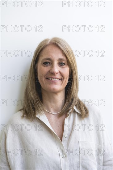 Beautiful mid aged woman looking at camera leaning on white wall