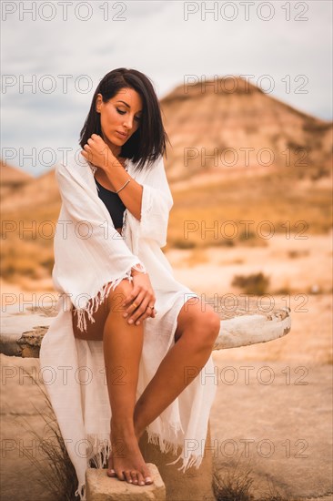 Lifestyle of a young brunette Caucasian girl in a white dress sitting in a beautiful desert