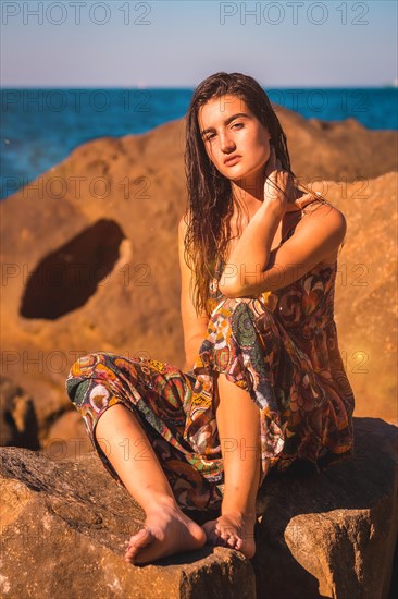 Portrait of a young brunette with wet hair and a floral dress by the sea