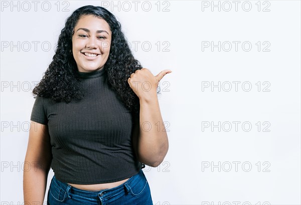 Smiling young woman pointing side with hand. Cheerful latin girl pointing an offer isolated. Happy latin woman pointing a promo isolated